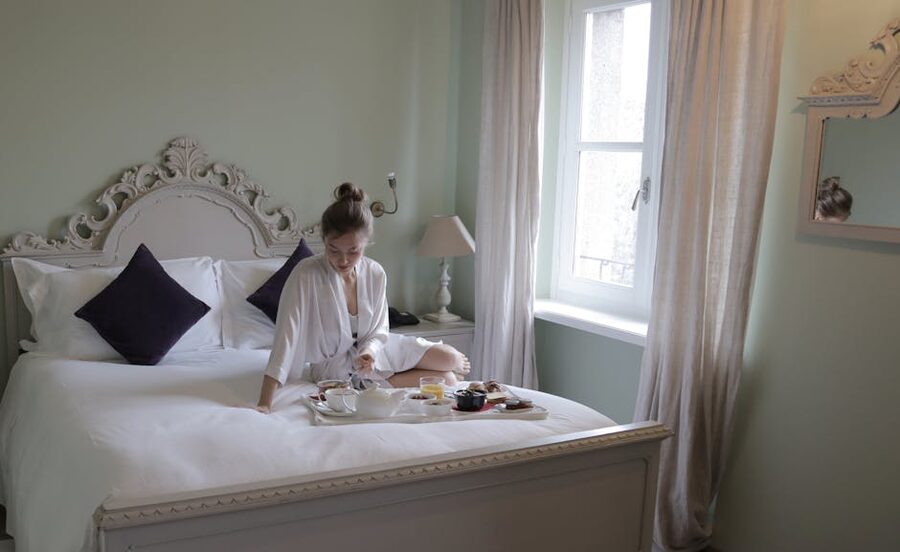 A woman in a robe enjoys a breakfast tray on a bed in a stylish hotel