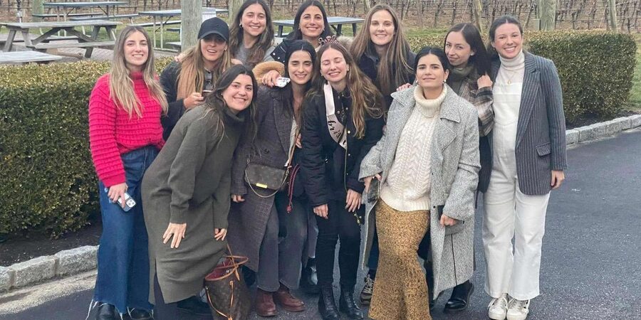 Bachelorette party of eleven women posed in front of a Long Island East End vineyard with picnic tables