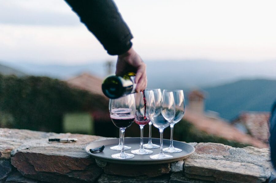 A wine flight tray with several glasses being poured outdoors