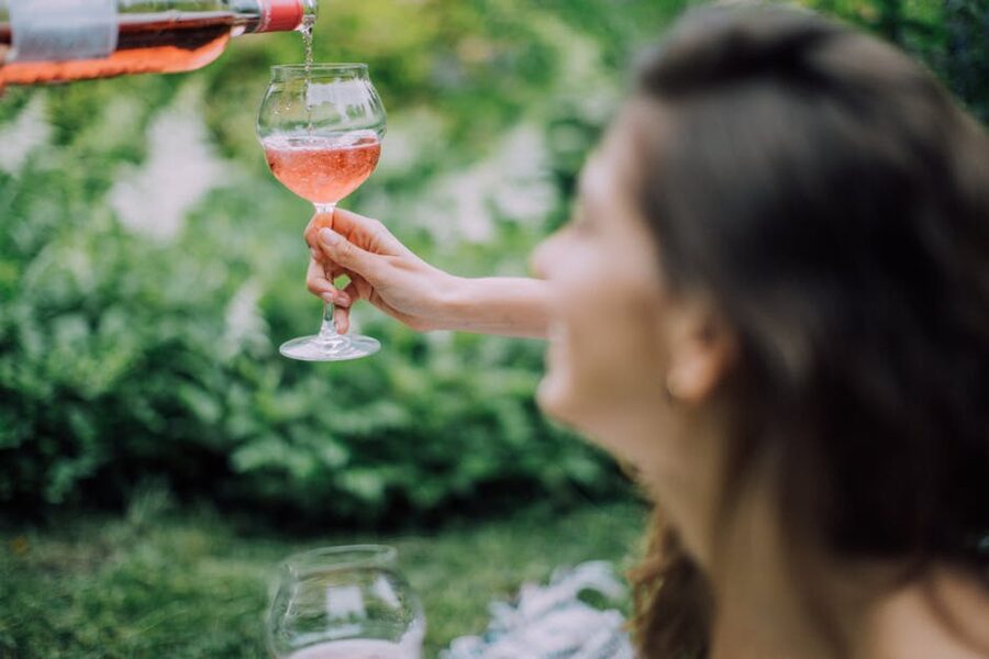A woman pouring rose wine into a glass during a sunny outdoor picnic
