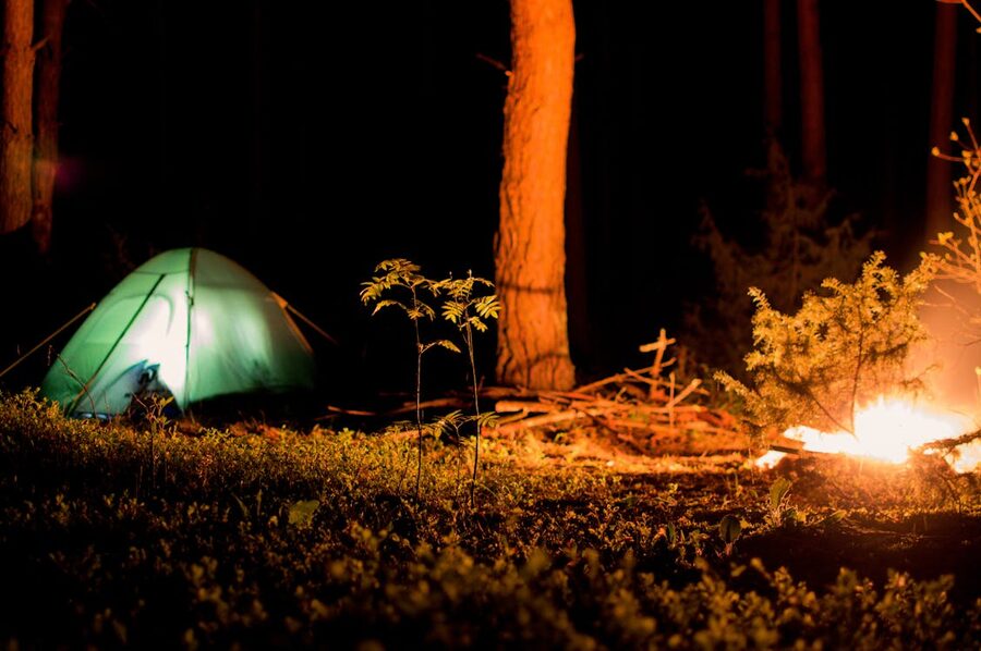 A tent and campfire glowing at night in the woods
